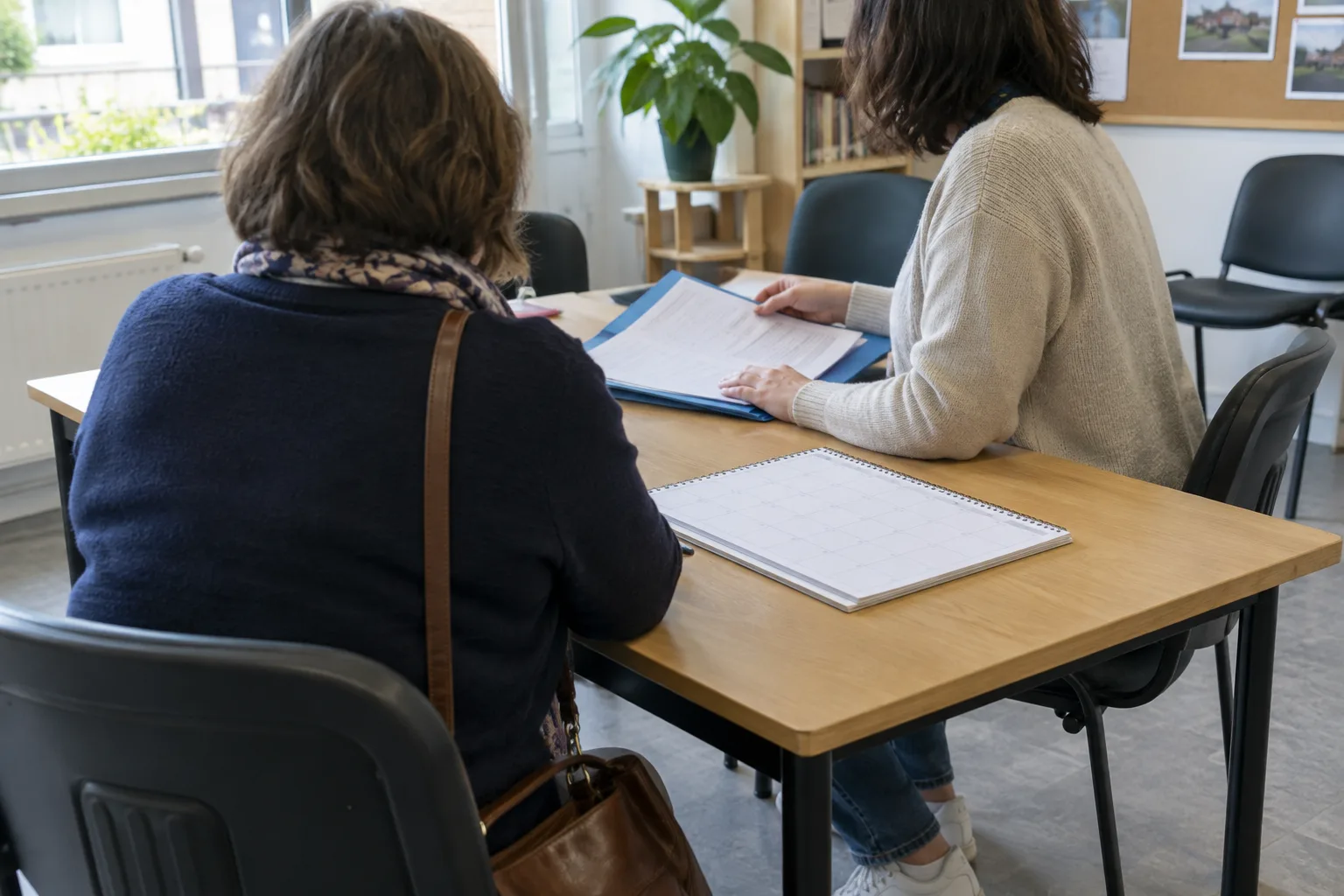 Dans une salle associative, deux personnes échangent autour d’un dossier posé sur une table.